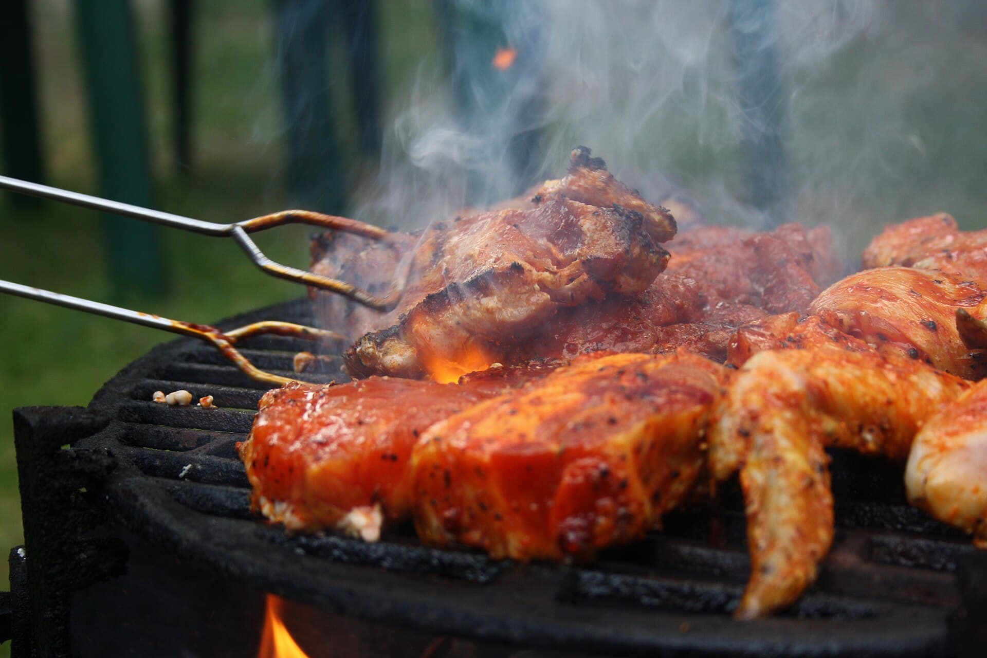 Two steaks being turned with long grill tongs on a hot charcoal barbecue