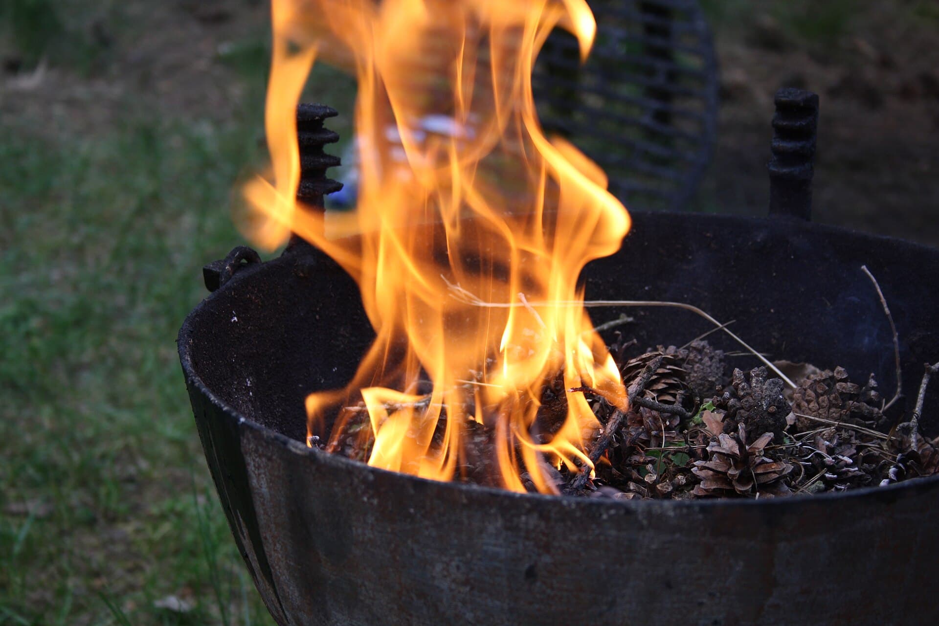 Tall orange flames rising from pine cones and dry twigs inside a black kettle barbecue