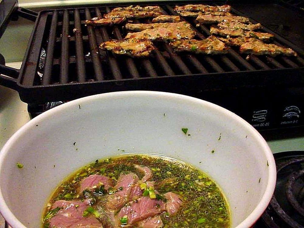 Sliced grilled steak coated in a dark marinade on a white plate